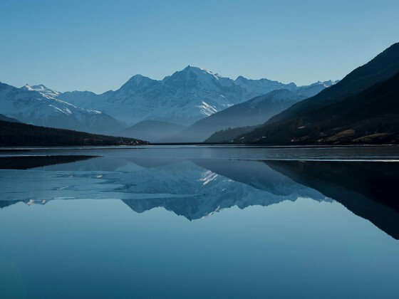 Das ist der Name des Bildes Mountain lake reflecting snow-capped peaks under blue sky
